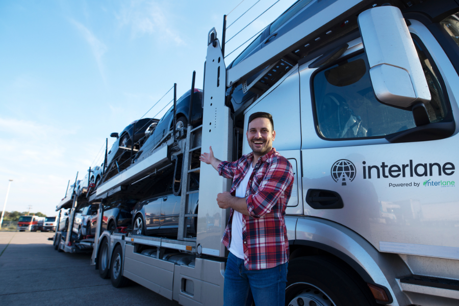 Smiling driver standing next to an Interlane car hauler loaded with vehicles, demonstrating the car shipping process.
