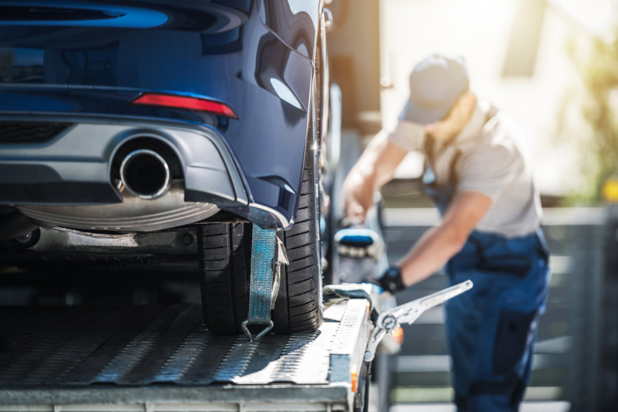 Close-up of a car being secured to a trailer by a worker during the vehicle shipping process.