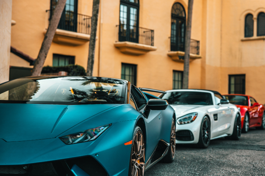Row of exotic sports cars including a teal Lamborghini and white Mercedes-Benz parked in front of upscale buildings, representing luxury vehicle transport in Canada.