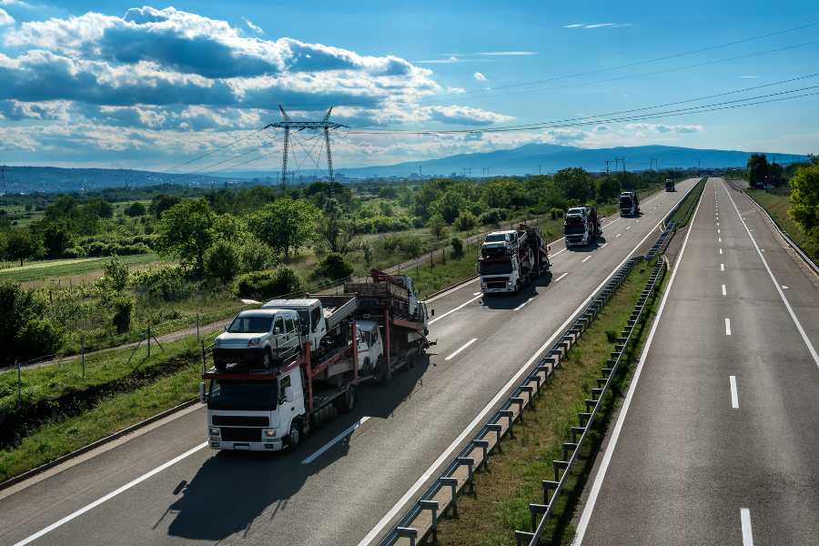 Multiple car carrier trucks transporting vehicles on a scenic highway under a blue sky, representing various car shipping methods.